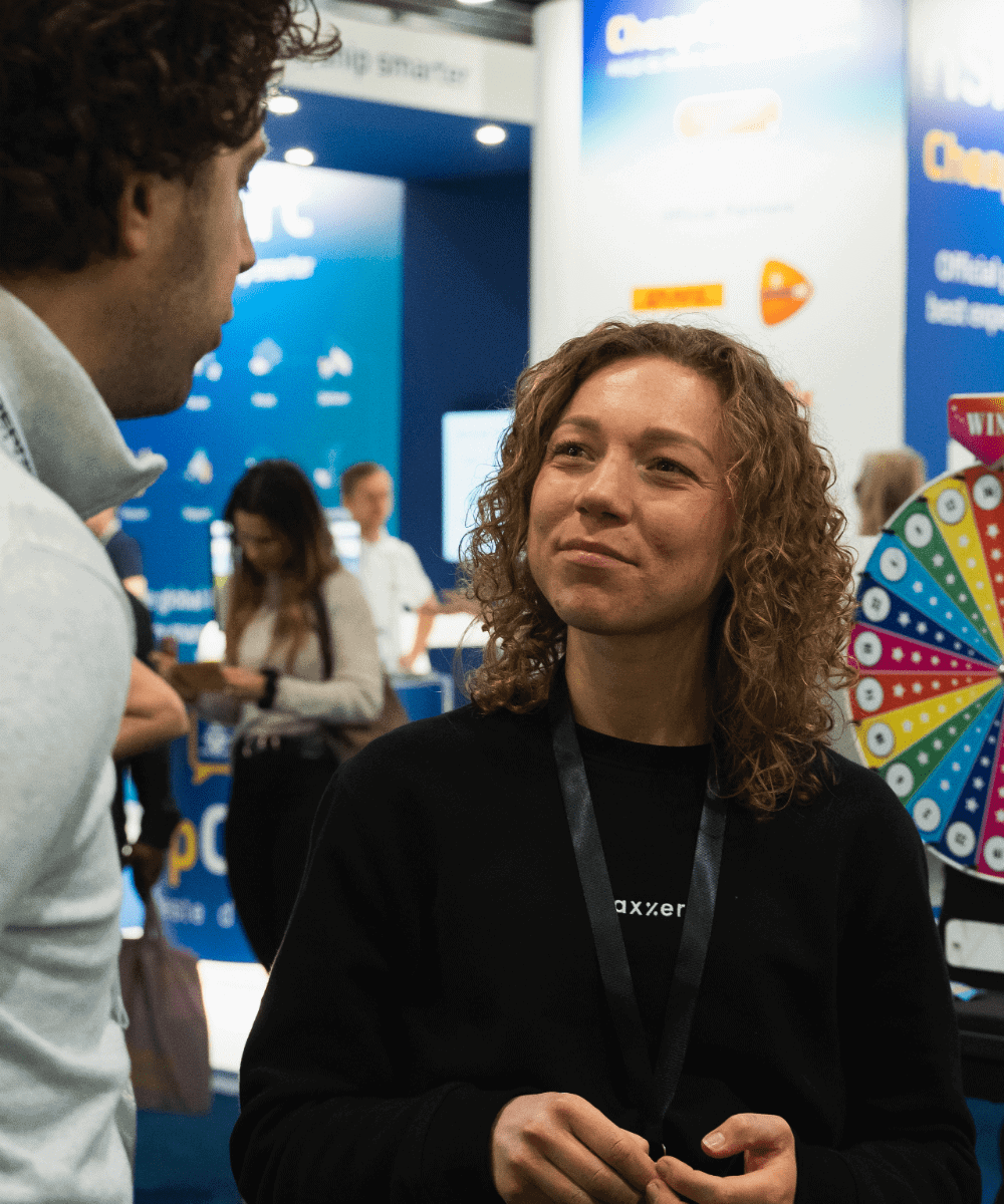 A woman engaging in a conversation with a man at a trade show, discussing vat registration.
